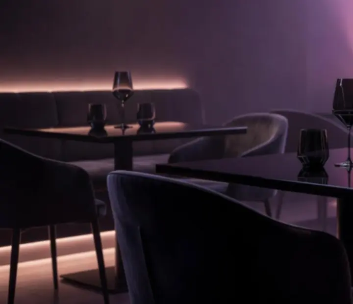 Atmosférická večerní restaurace Bravoriaim s tmavým osvětlením a fialovo-růžovým nádechem.